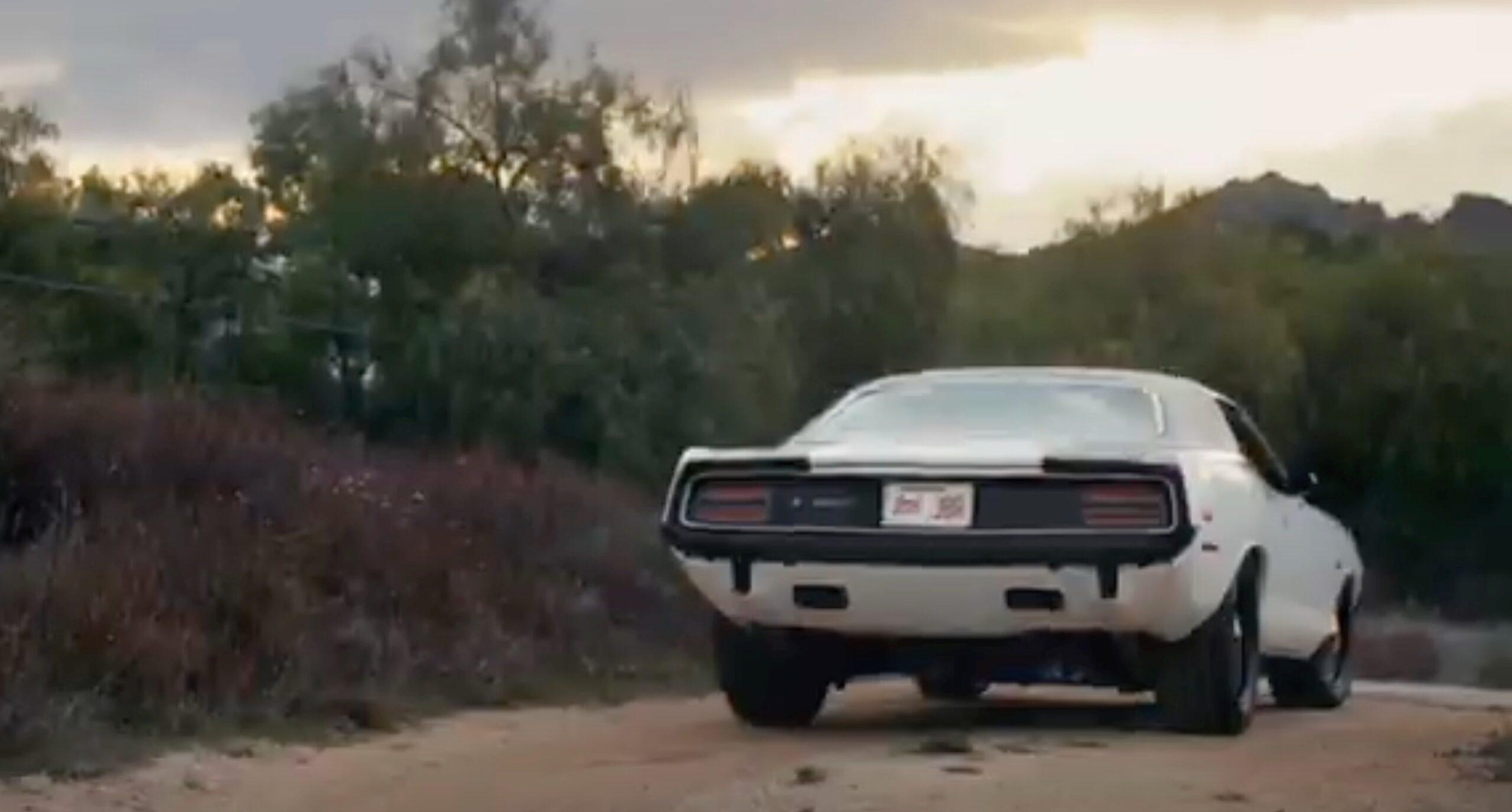 A white muscle car driving down a dirt road.