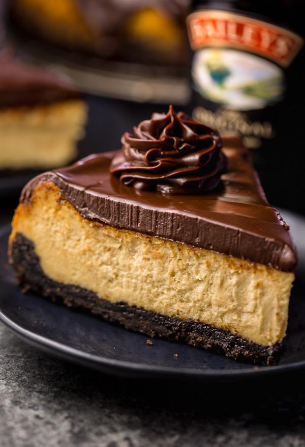 Slice of baileys cheesecake on a black plate with chocolate ganache on top.