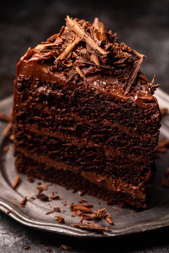 Slice of devil's food cake on a silver plate topped with chocolate shavings.