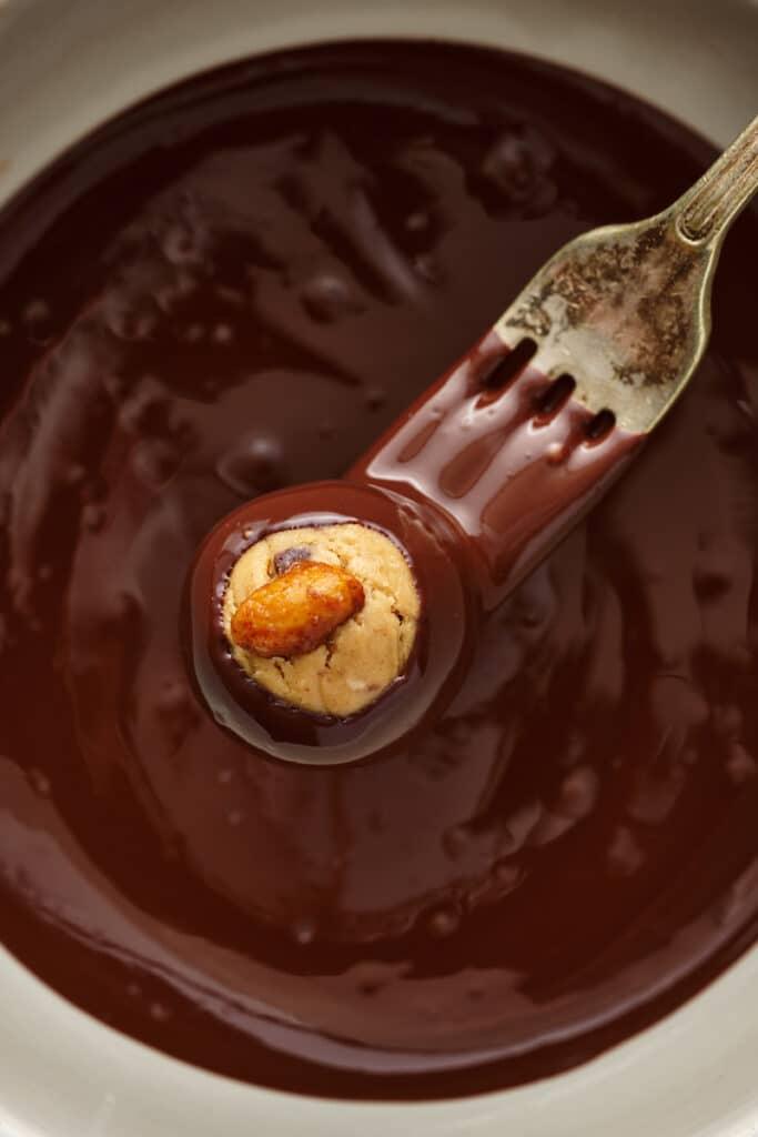 Fork dipping the buckeyes into the dark chocolate coating.