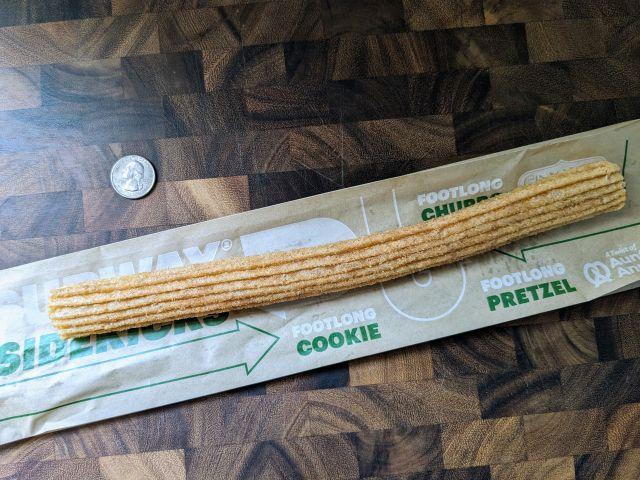 A Subway Footlong Churro next to a quarter.