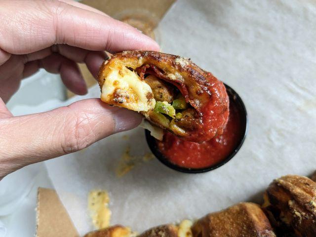 A Papa Johns Calzone Papa Bite dipped in pizza sauce.