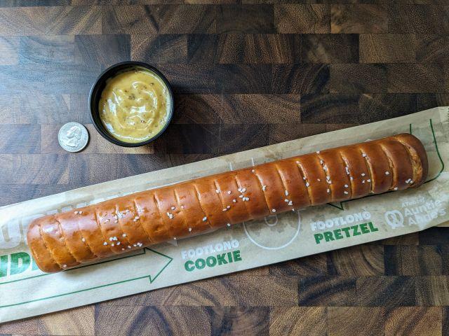 Subway's Footlong Pretzel next to a quarter and honey mustard dipping cup.