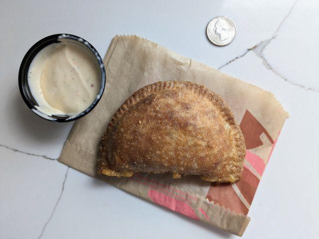 Taco Bell's Cheesy Chicken Crispanada next to Spicy Ranch dipping sauce cup.