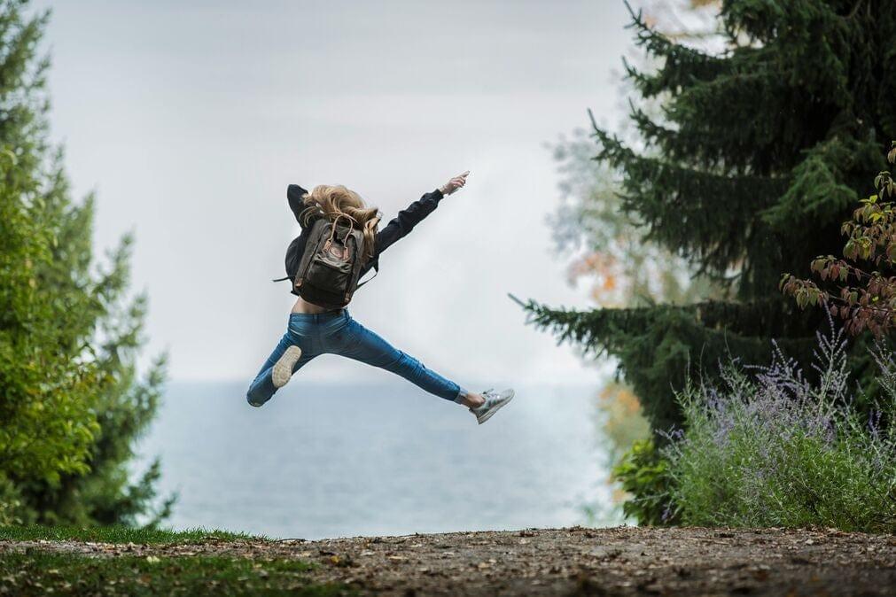 A young woman hiking in a scenic rural secene, jumping for joy and with ease.