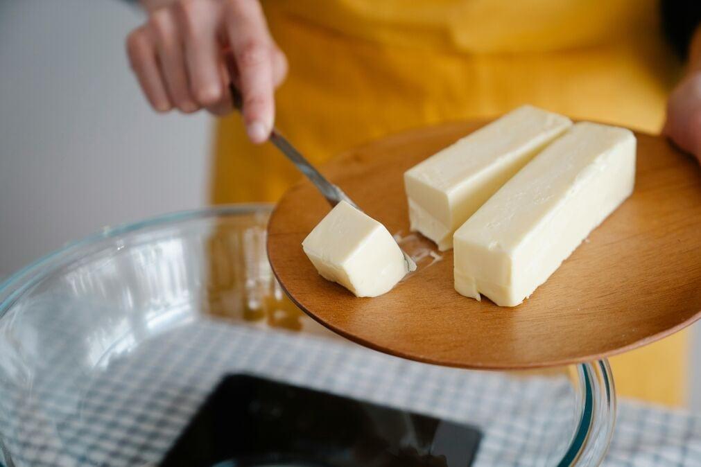 Sticks of butter being cut on a wooden chopping board.