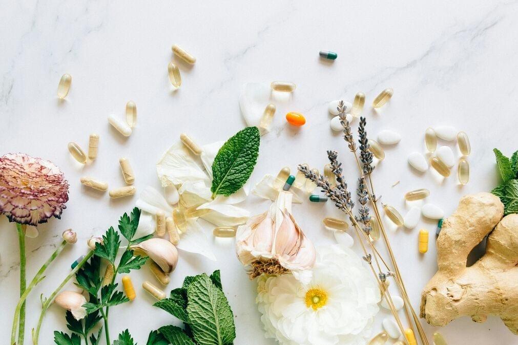 A selection of supplementds and anti-inflammatory ingredients scattered on a marble worktop with white flowers.