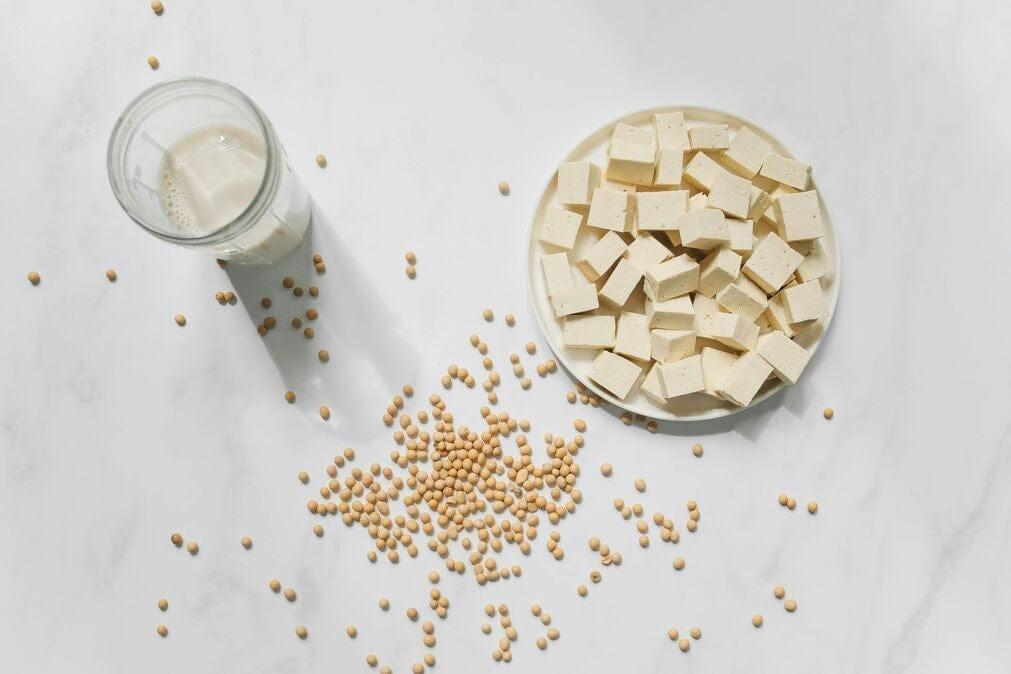 A selection of soy products on a white background, including dried soy beans, tofu and soy milk, all of which are clean vegan protein sources.