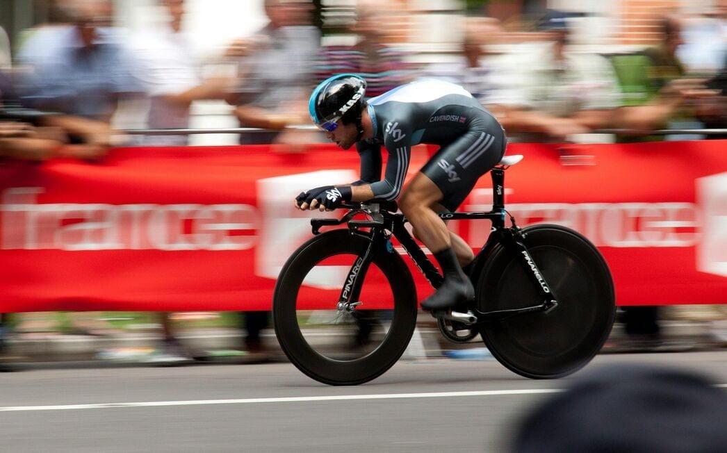 A professional cyclist riding for Team Sky in an aero tuck position over their handlebars and going at fast speed.