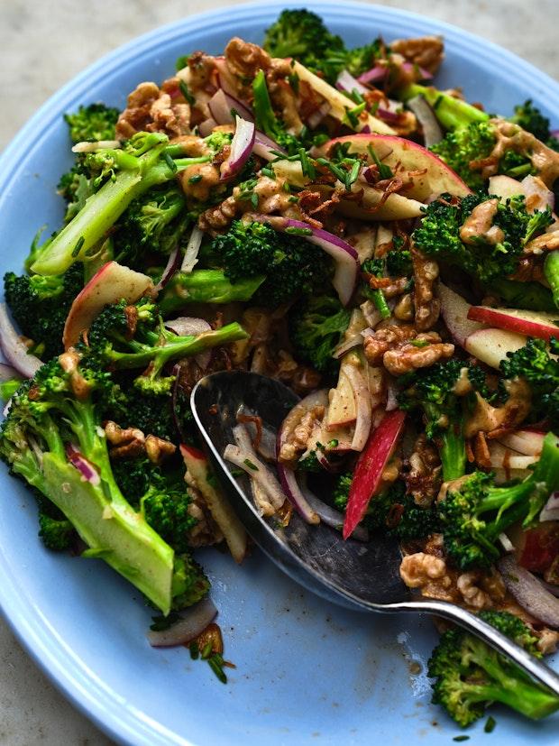 broccoli apple salad drizzled with dressing on a blue plate with a large serving spoon