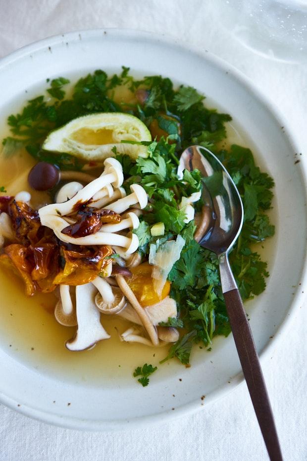 bowl of tom yum soup topped with tomatoes, mushrooms and lime wedge