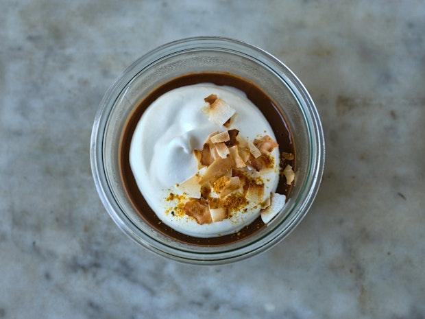 chocolate pudding in a glass bowl with whipped cream and toasted coconut on top