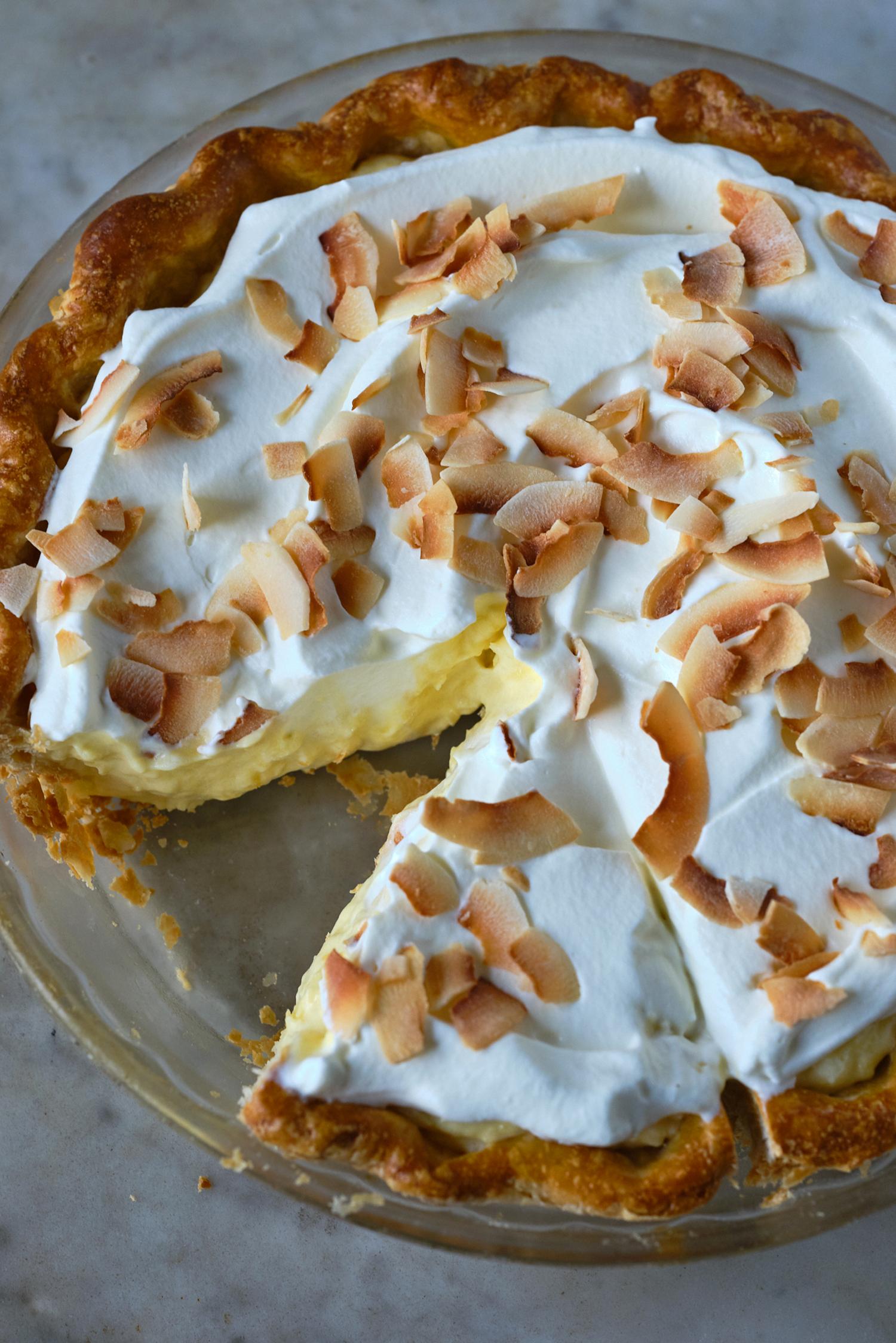 coconut cream pie in a glass pie plate with a slice cut out of it