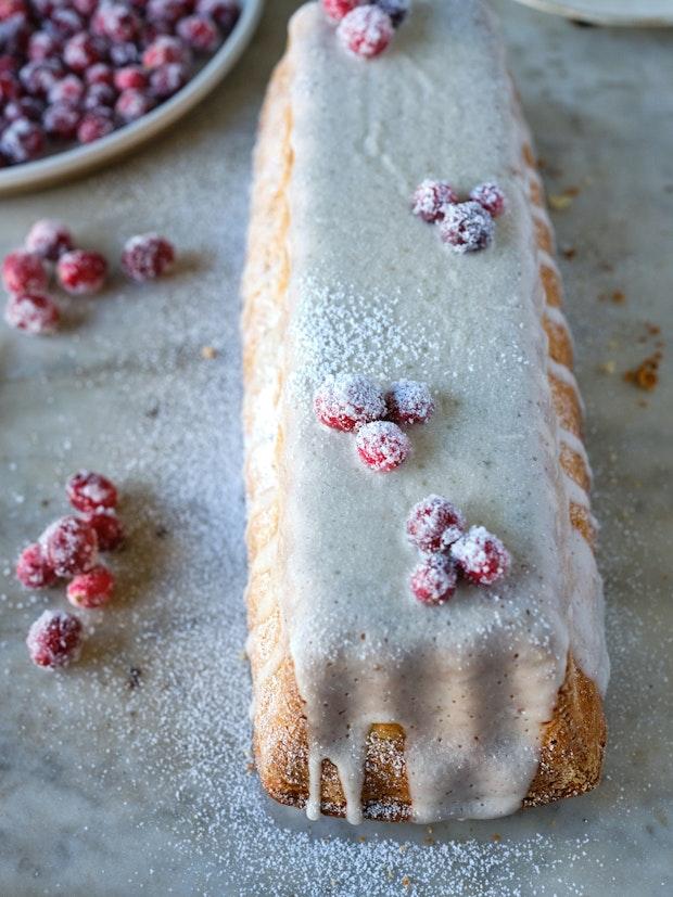 A cranberry cake with vanilla icing decorated with sugared cranberries on a table