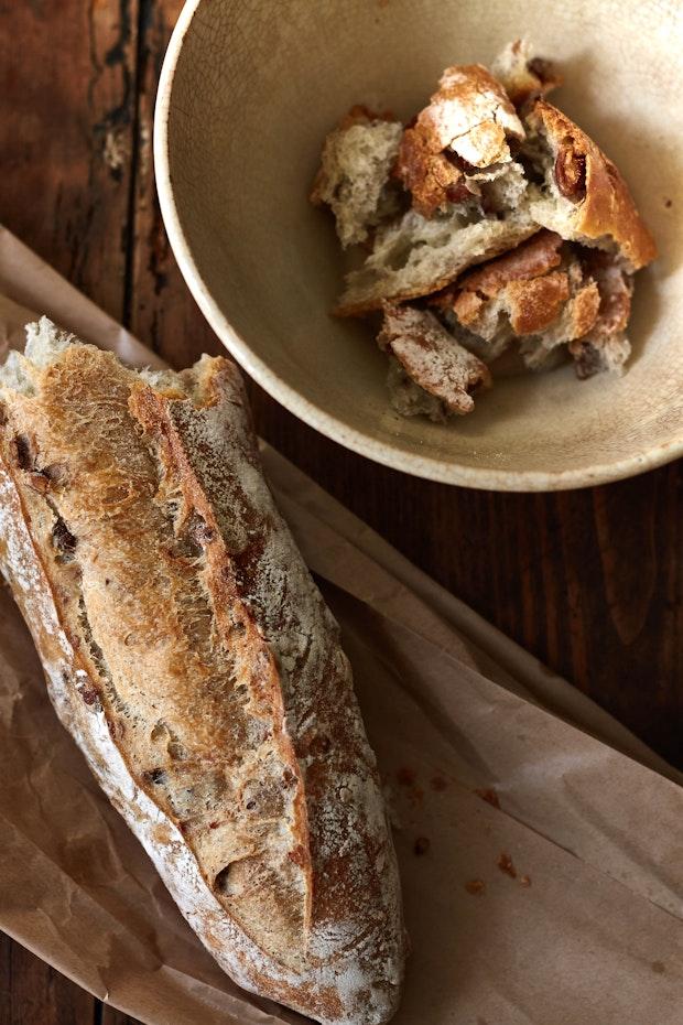 half a baguette on a paper bag alongside some torn baguette in a bowl