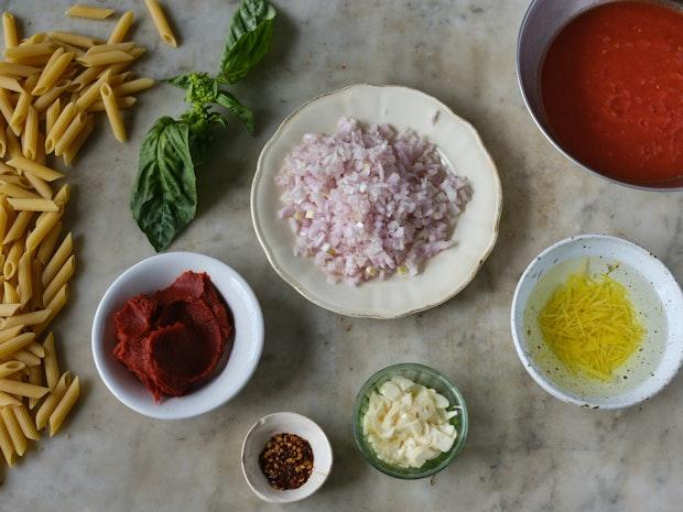 ingredients for cooking penne alla vodka including tomato paste, dried pasta, basil, and garlic