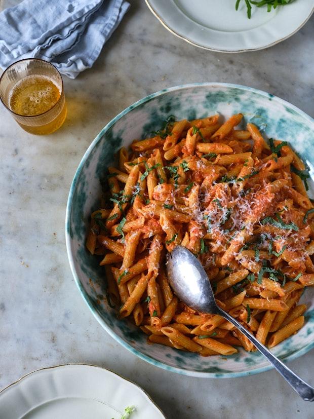 penne alla vodka being served on a marble table set with plates and a cloth napkin