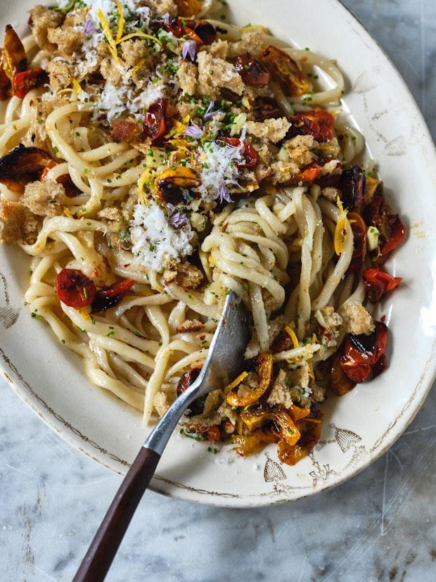 Pici on a white plate with garlic, tomatoes, breadcrumbs and chives