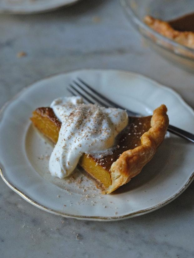 a spice of pumpkin pie on a plate with a golden crust and dollop of whipped cream