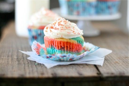 red white and blue cupcake with peeled cupcake liner all topped with frosting and sprinkles