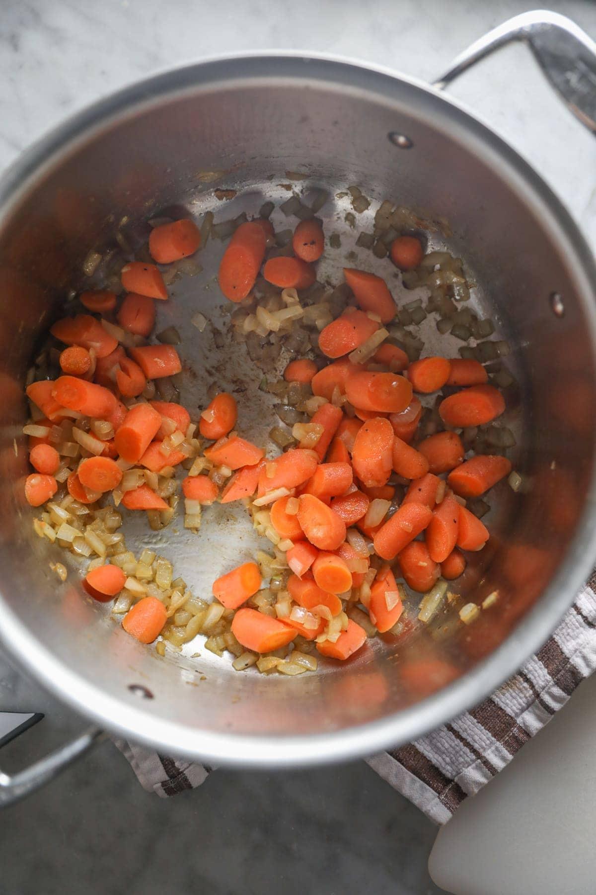 A pot on the stove of onions and carrots