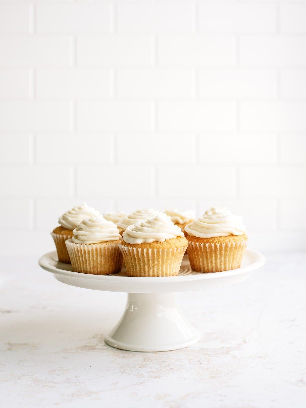 frosted vanilla cupcakes on a white cake platter