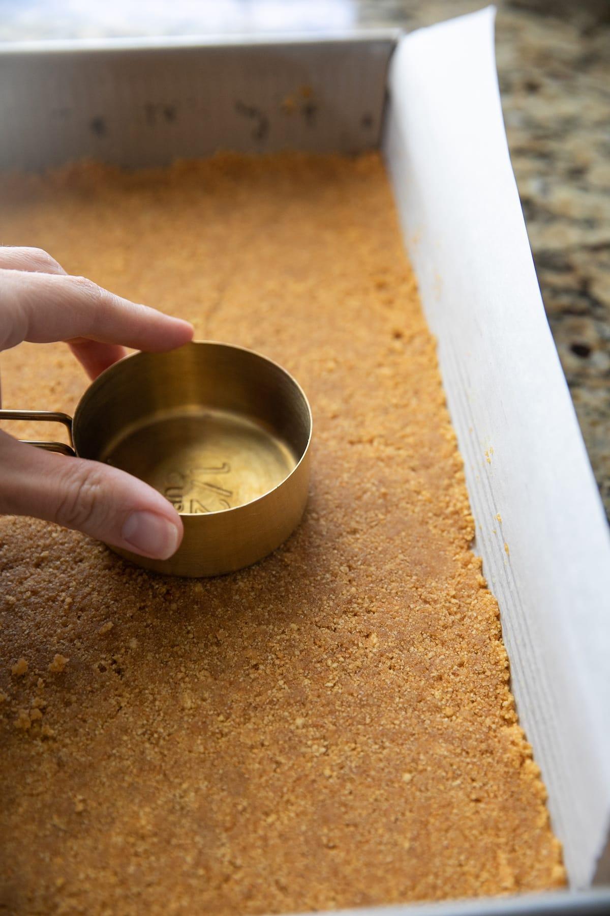 pressing down graham cracker crumbs with the back of a measuring cup