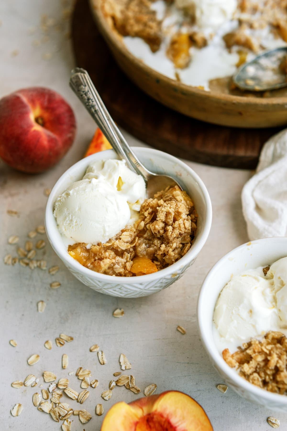 peach-crisp in bowl with spoon and ice cream