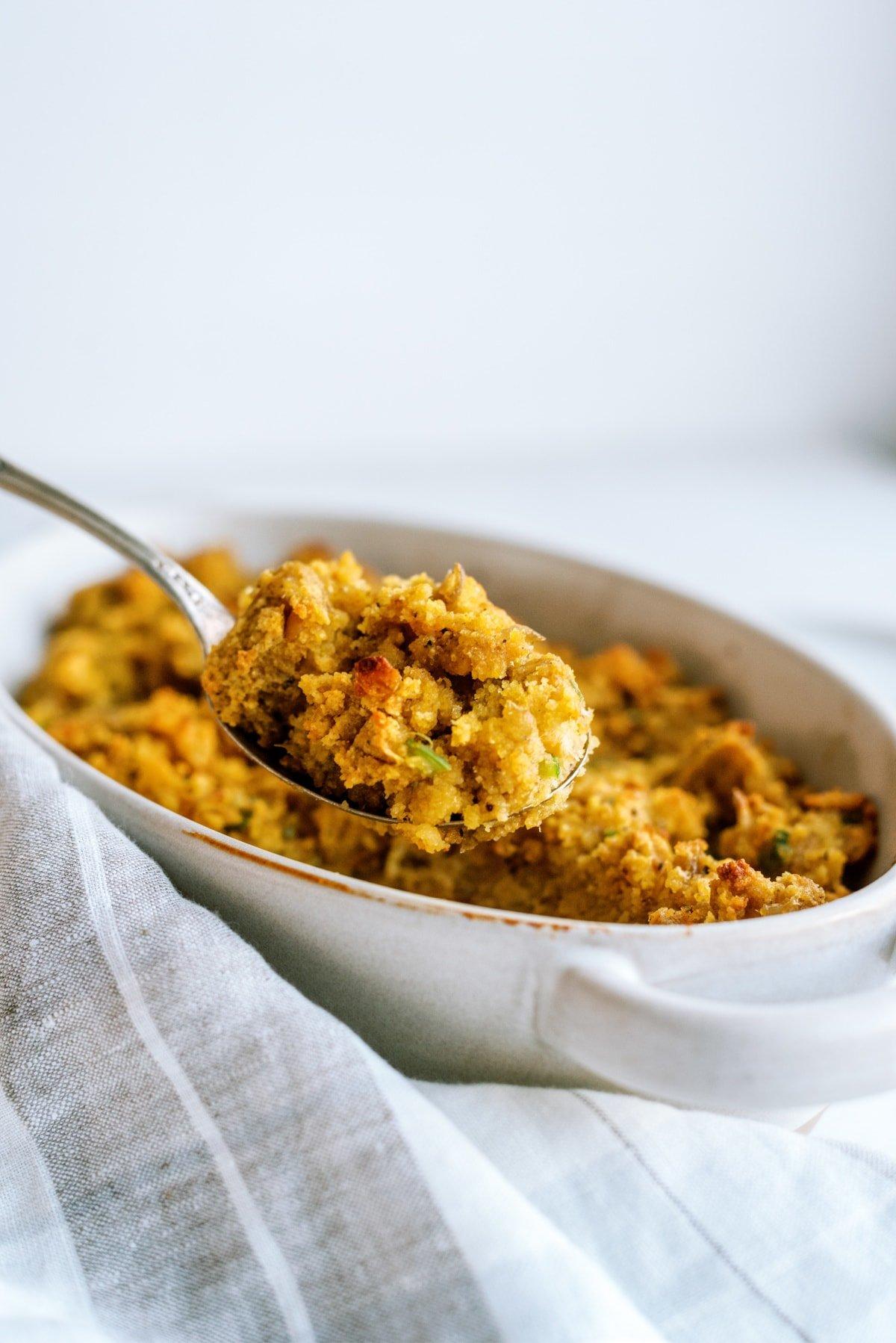 cornbread stuffing in dish being scooped out with serving spoon