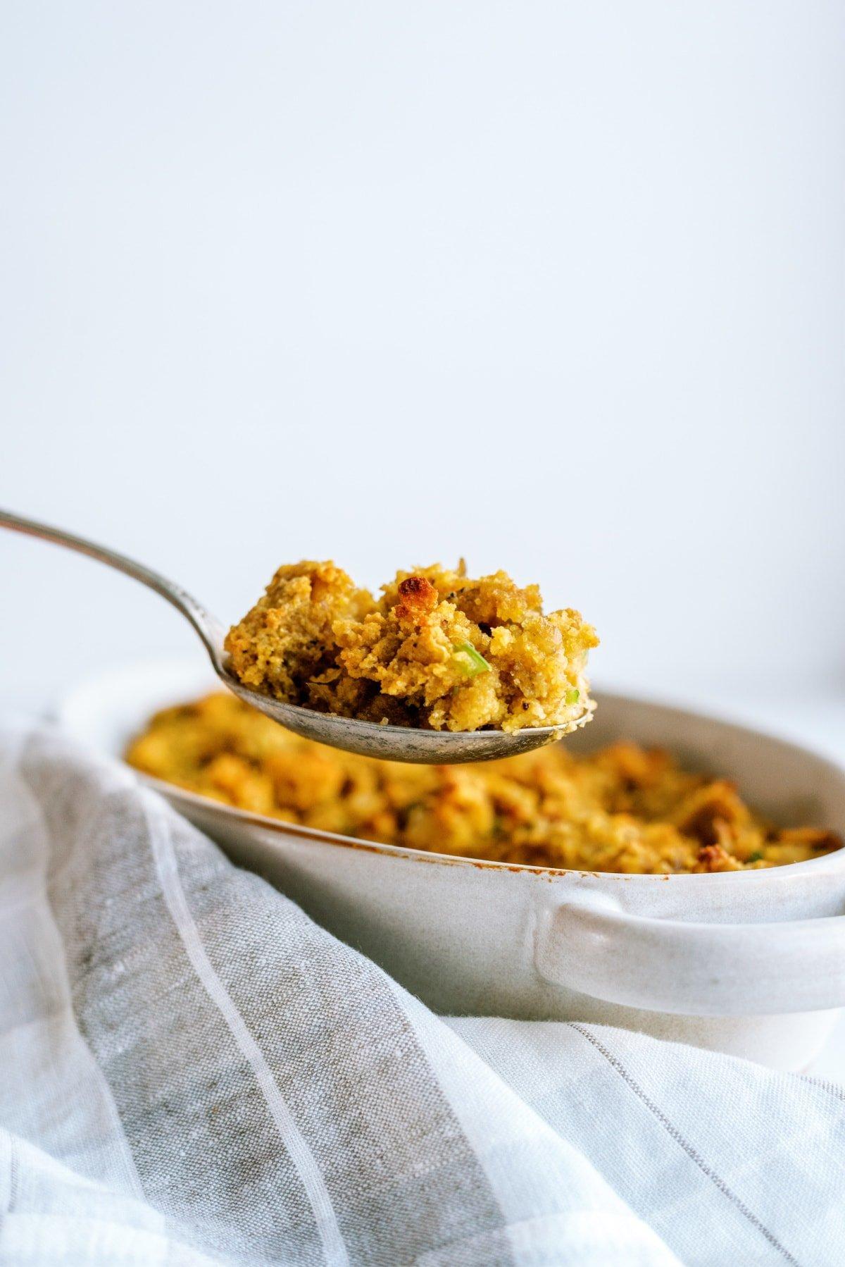 cornbread stuffing in dish being scooped out with serving spoon