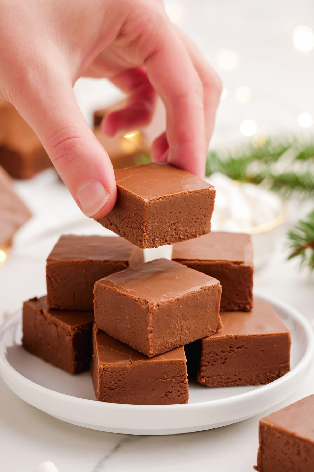 cubed fudge stacked on a plate with a hand adding one more cube