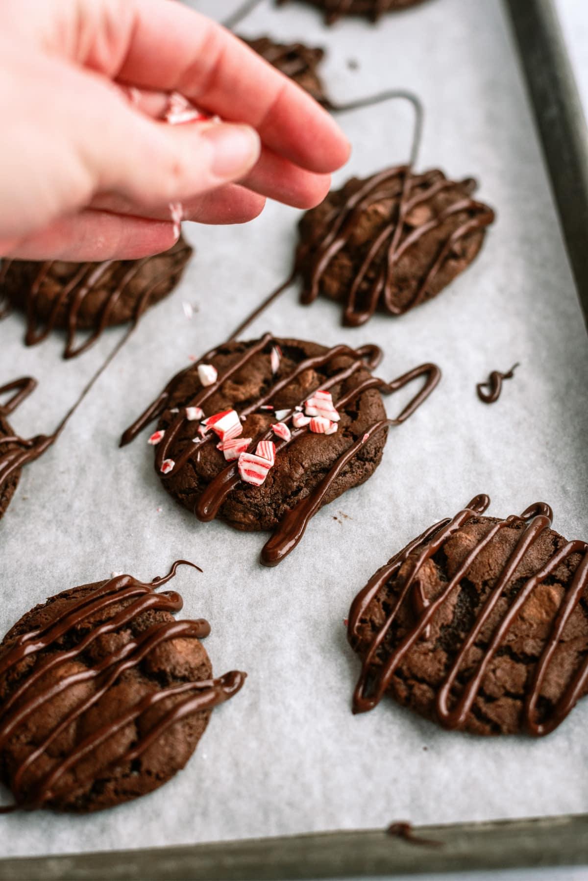 triple-chocolate-candy-cane-cookies with woman's hand sprinkling candy cane pieces on top