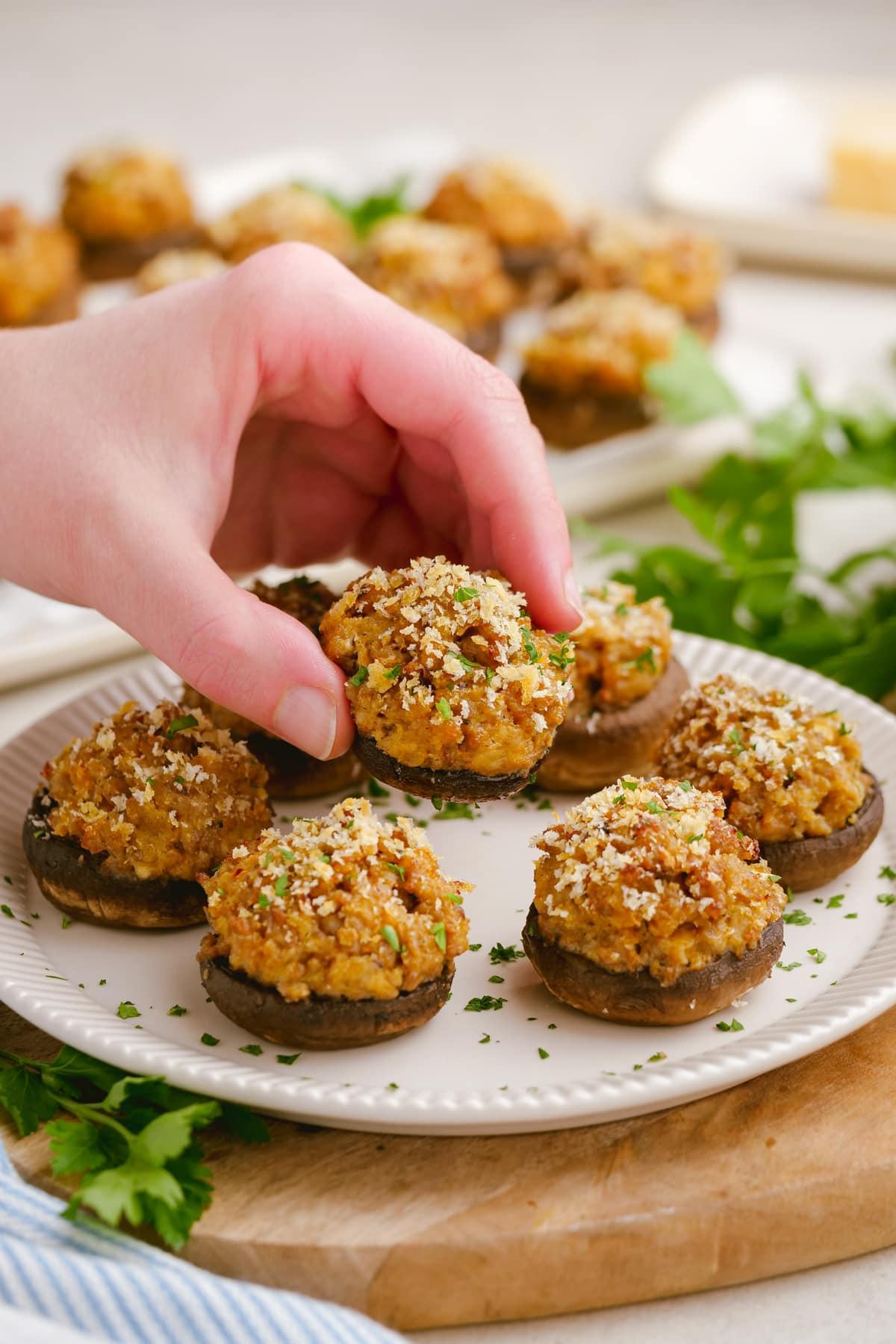 sausage stuffed mushrooms 21 woman's hand picking up cooked sausage-stuffed-mushrooms on plate