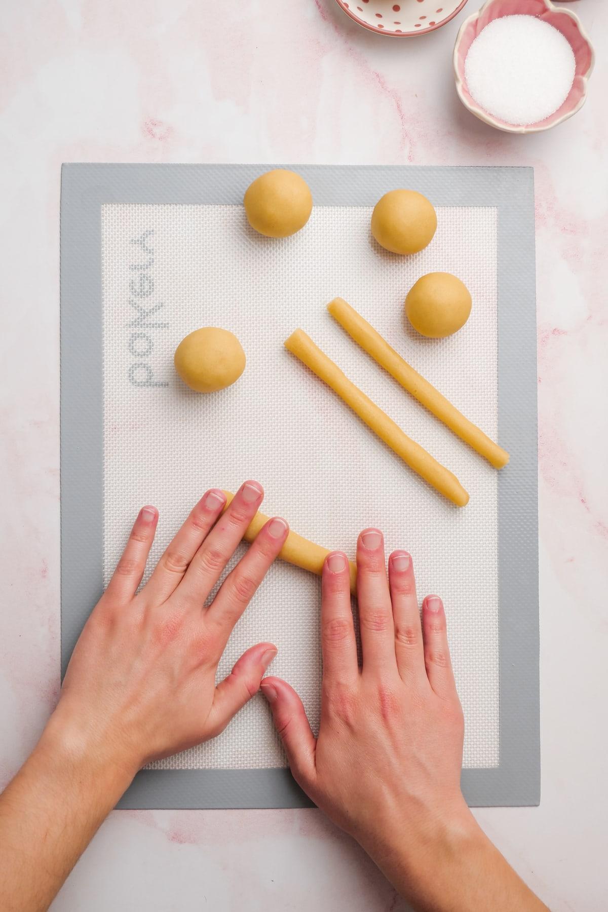 woman's hands rolling dough into skinny "snakes"