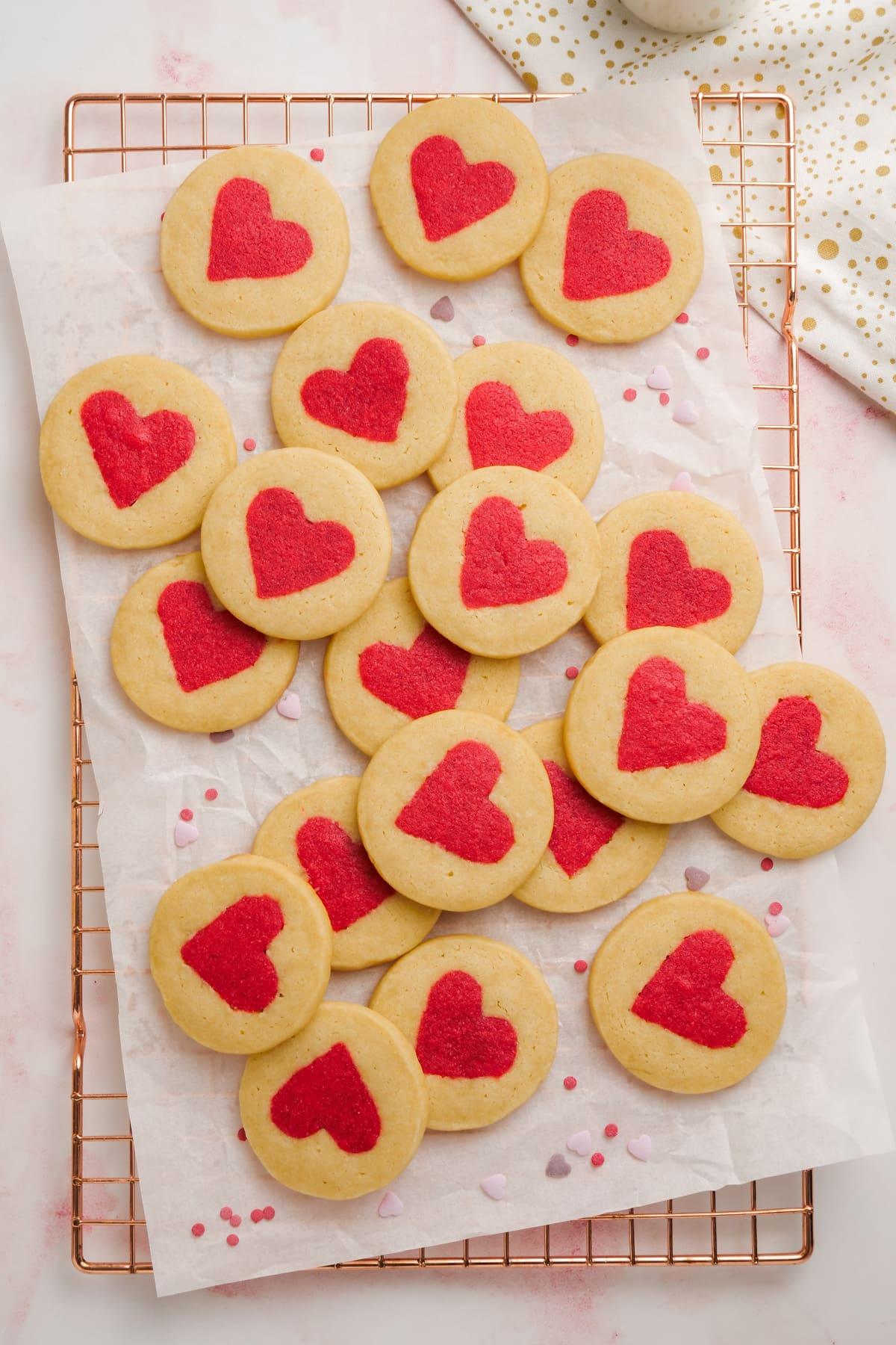 white cookies with red hearts in the middle spread out on parchment paper and cooling rack