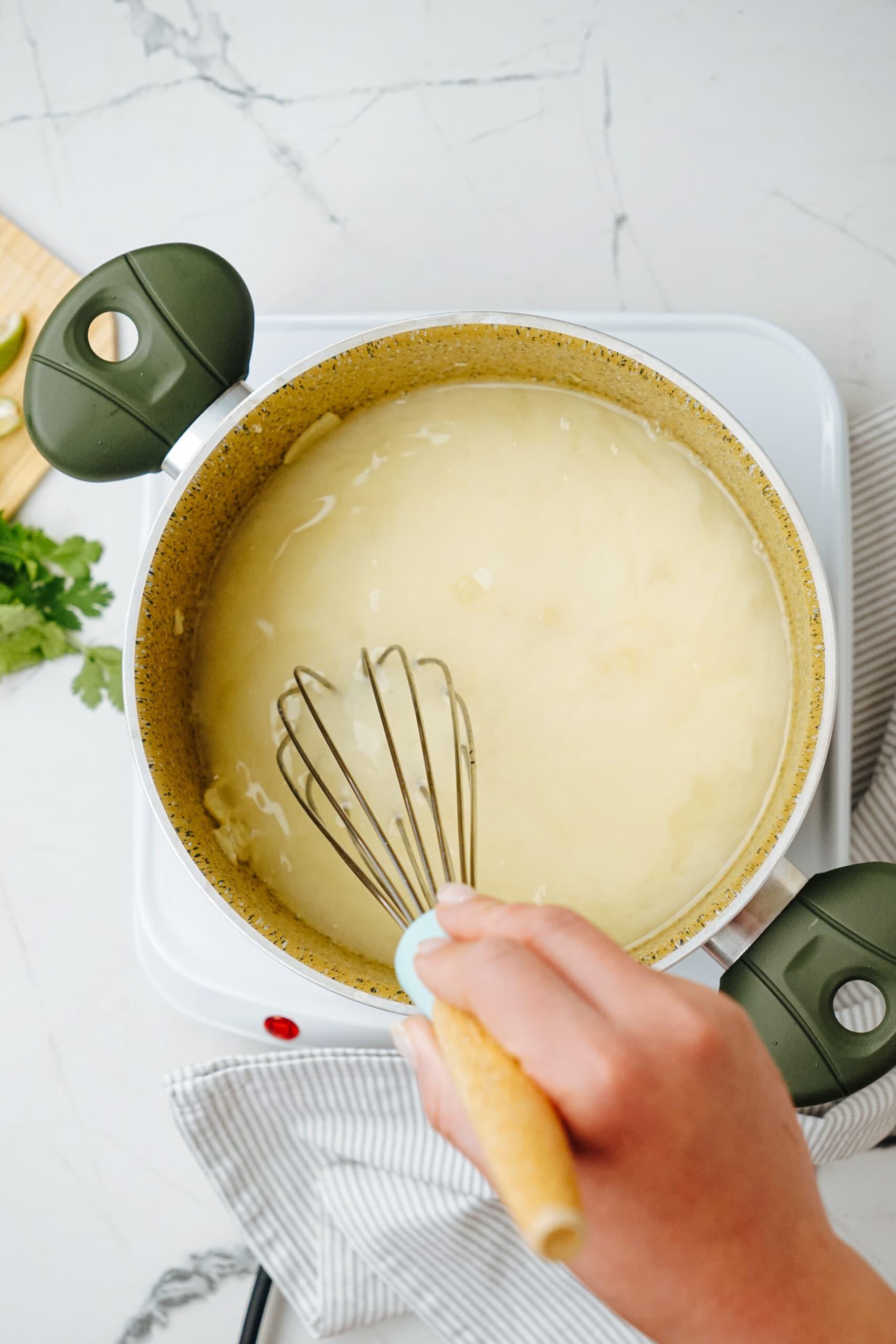 woman's hand whisking white chicken chili in pot