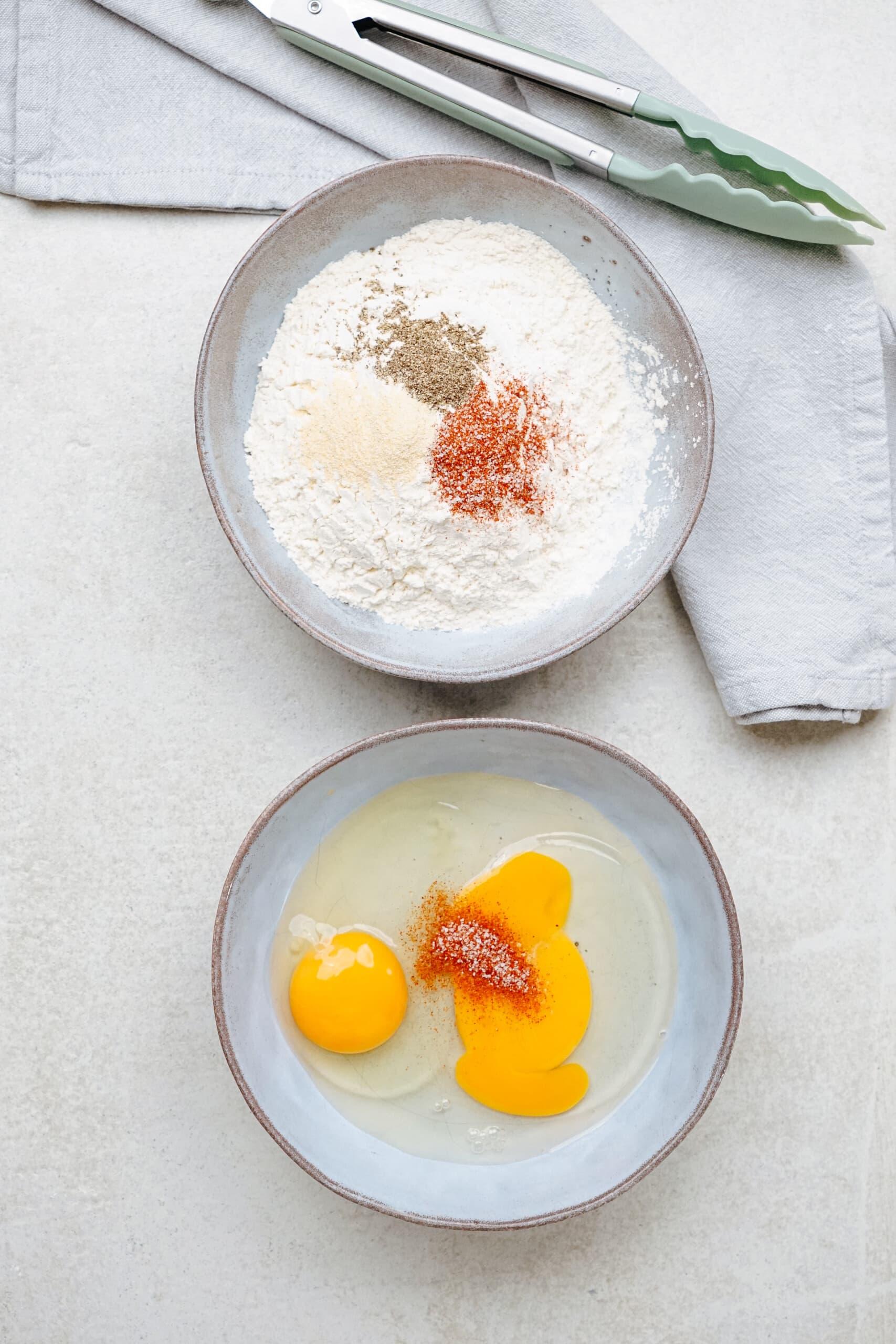 2 bowls, one with eggs and seasoning, the other with flour and seasonings