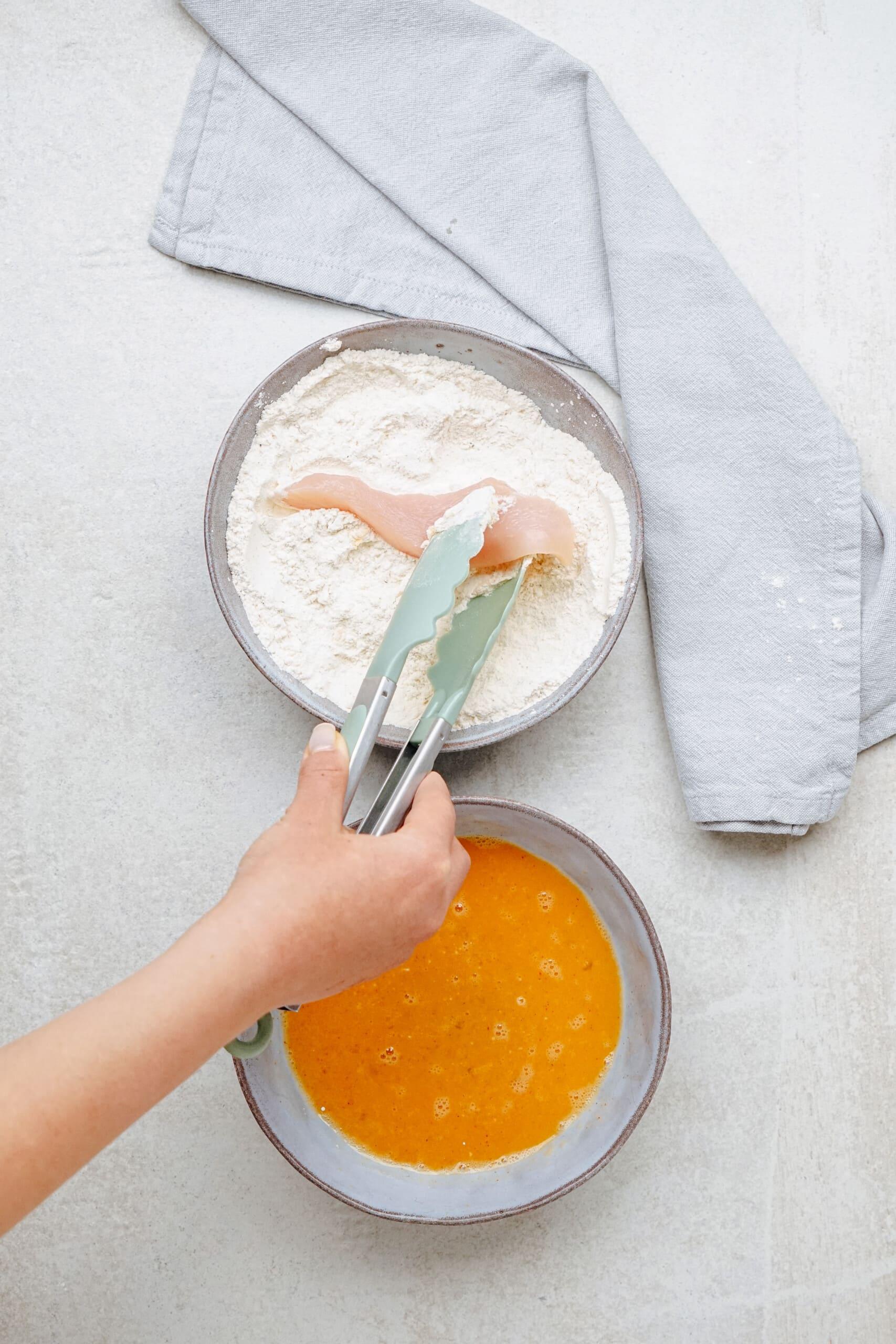 woman's hands using tongs to coat chicken in flour