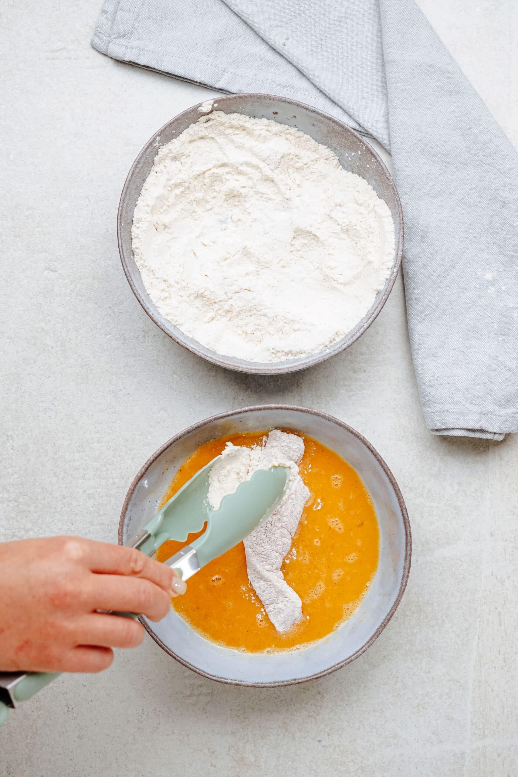 woman's hand using tongs to coat chicken in egg mixture