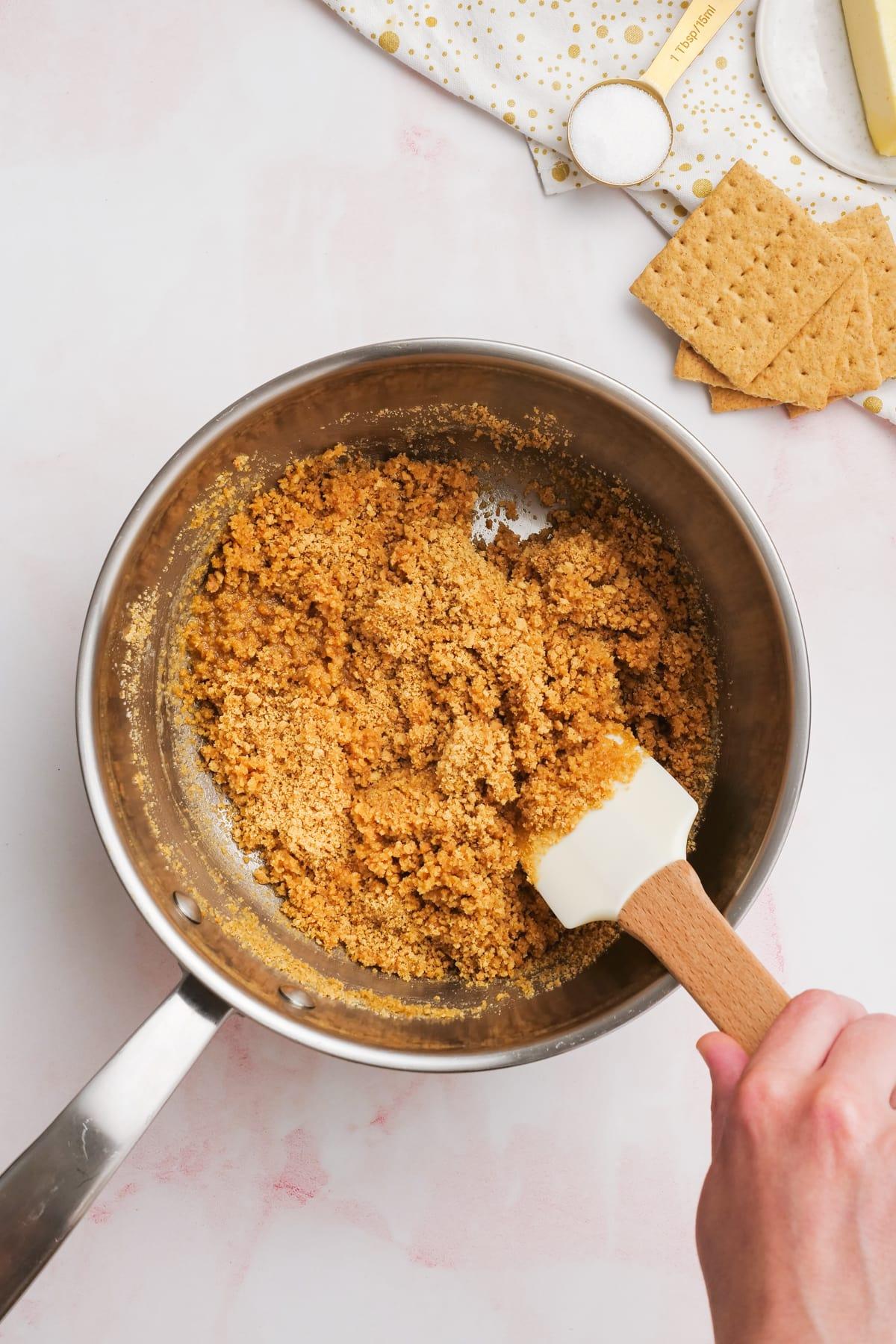 graham cracker crumbs being mixed into melted butter with a rubber spatula