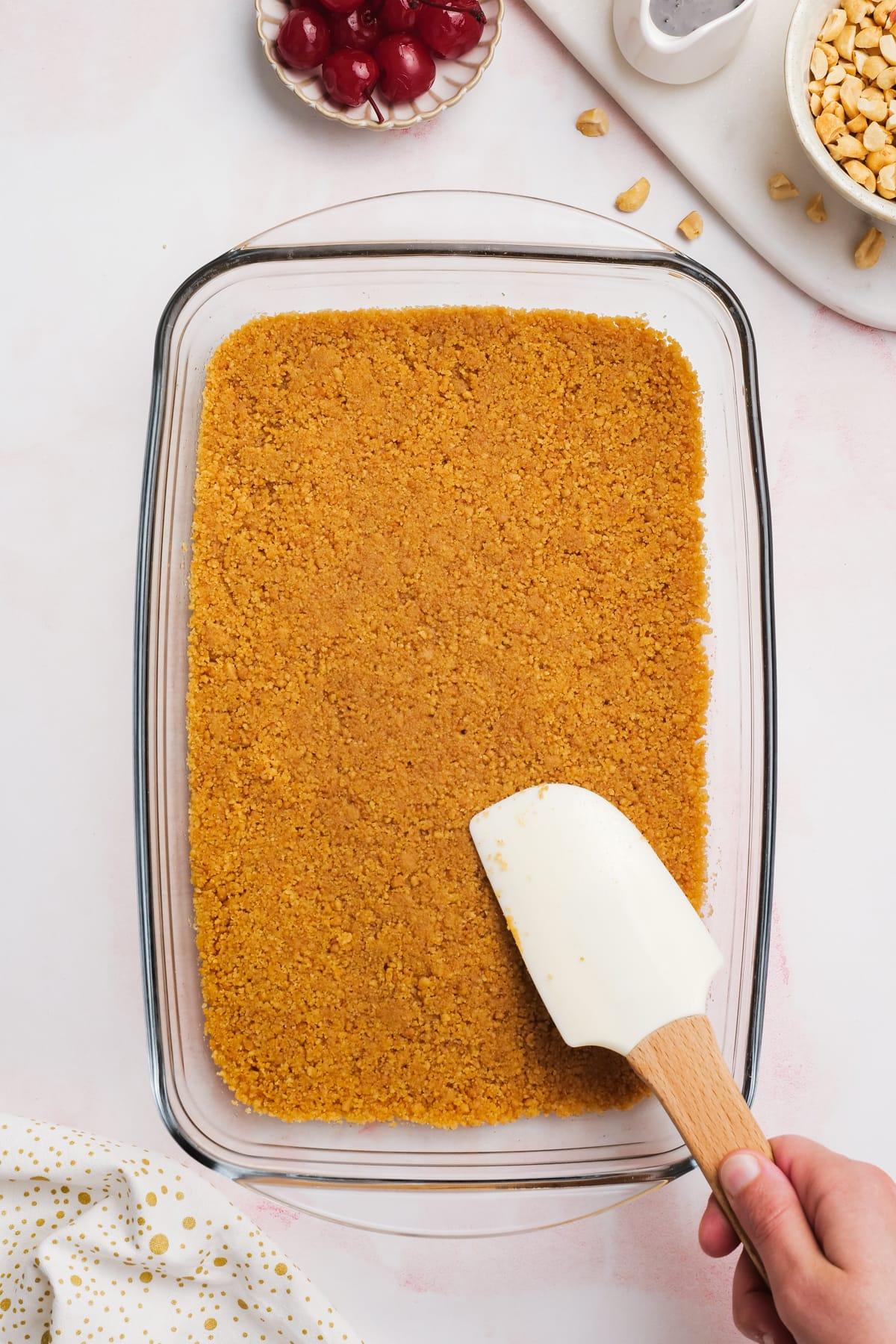 rubber spatula pressing graham cracker crust into baking dish