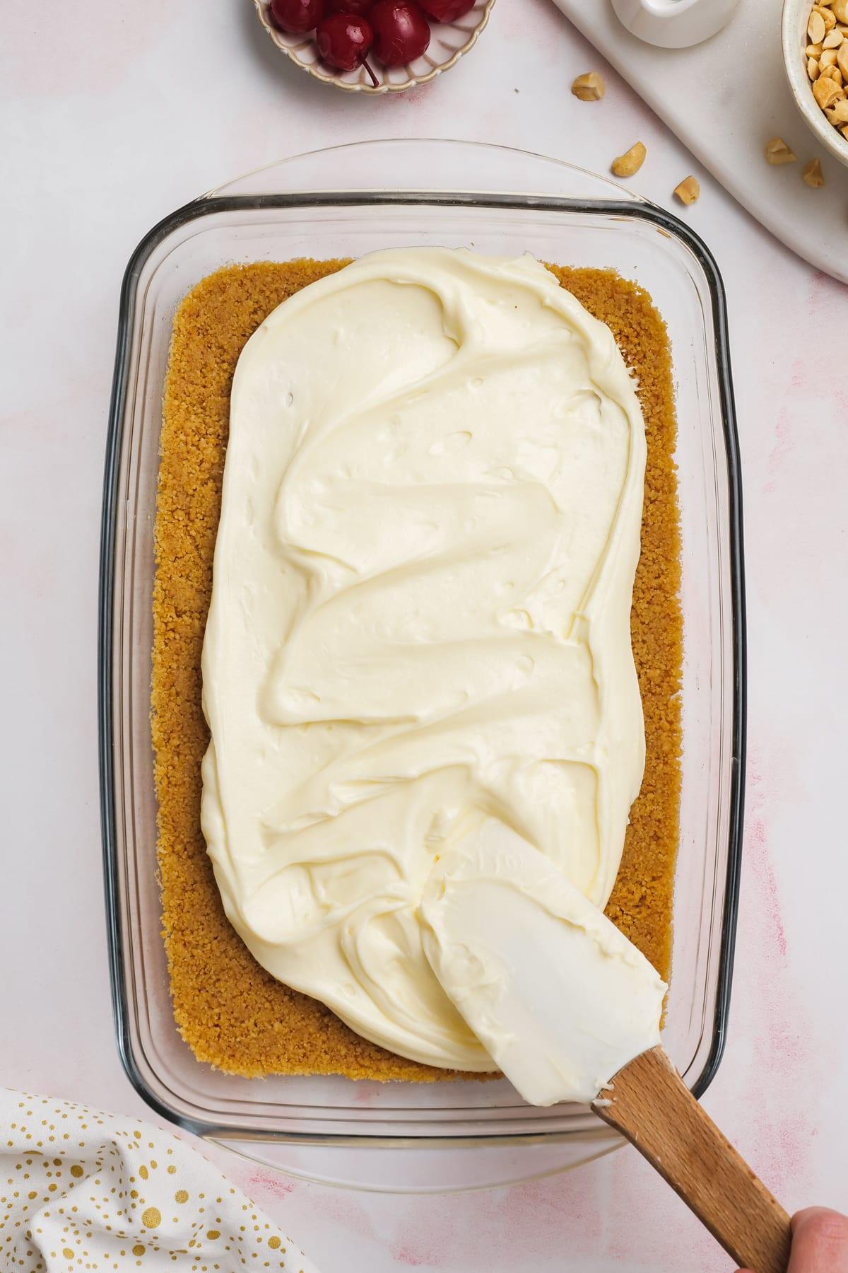 rubber spatula spreading cream cheese layer onto graham cracker crust layer