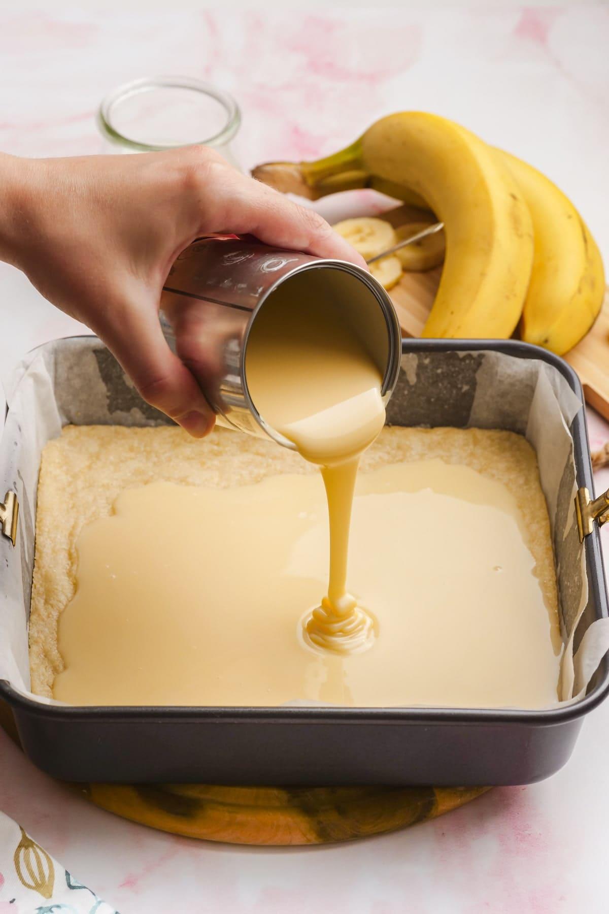 sweet and condensed milk being poured over shortbread crust