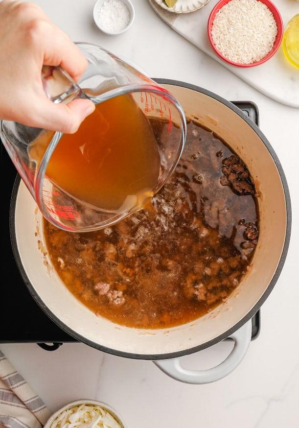 woman's hand pouring broth into pot