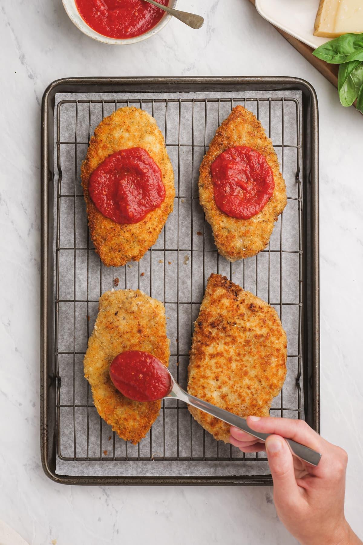 chicken breasts with a dollop of marinara sauce on each one, on a cooling rack and baking sheet