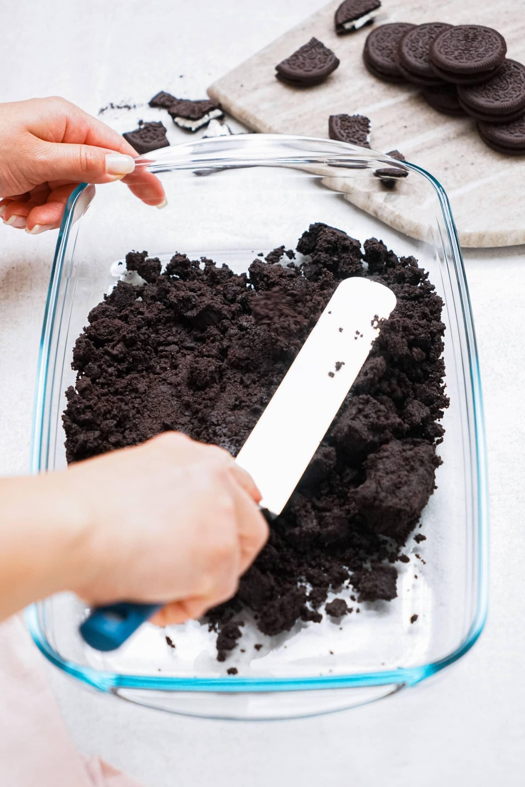 spatula pressing Oreo mixture into baking dish