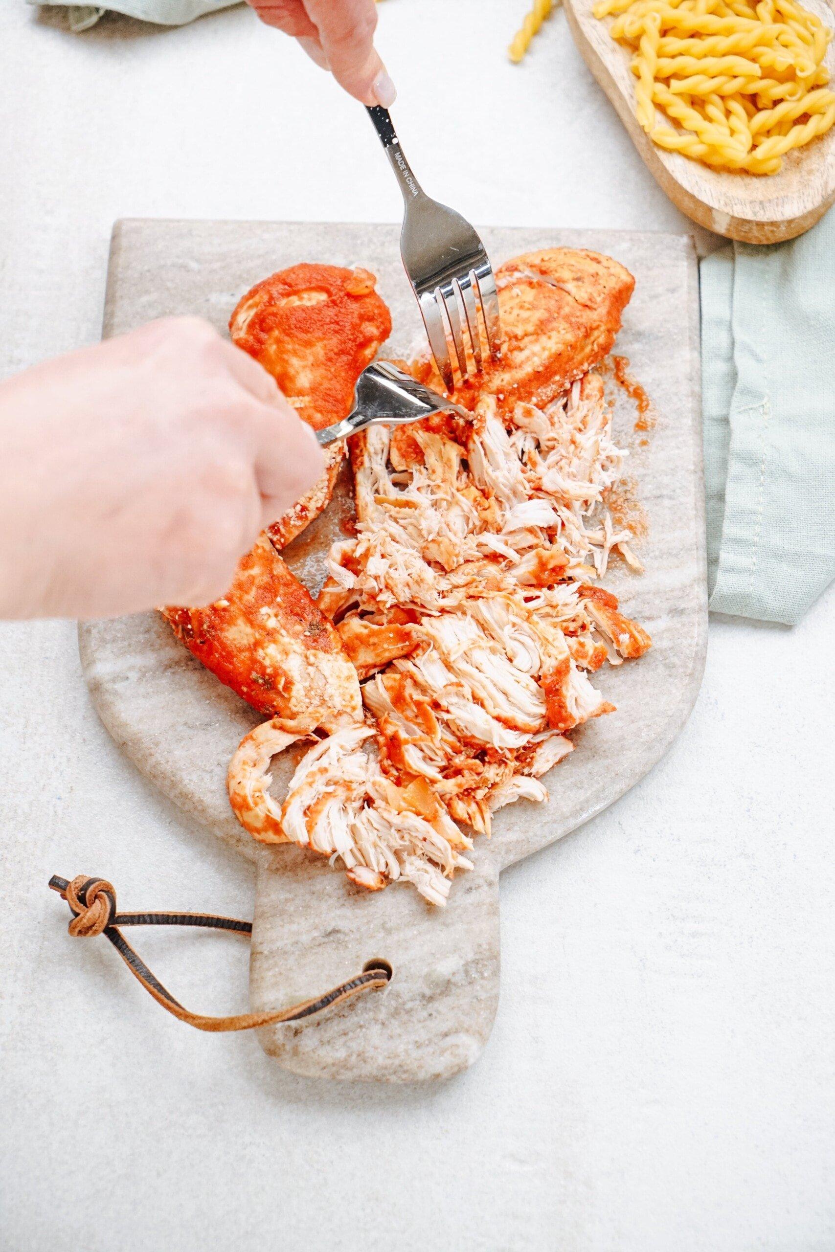 woman's hands shredding chicken with 2 forks