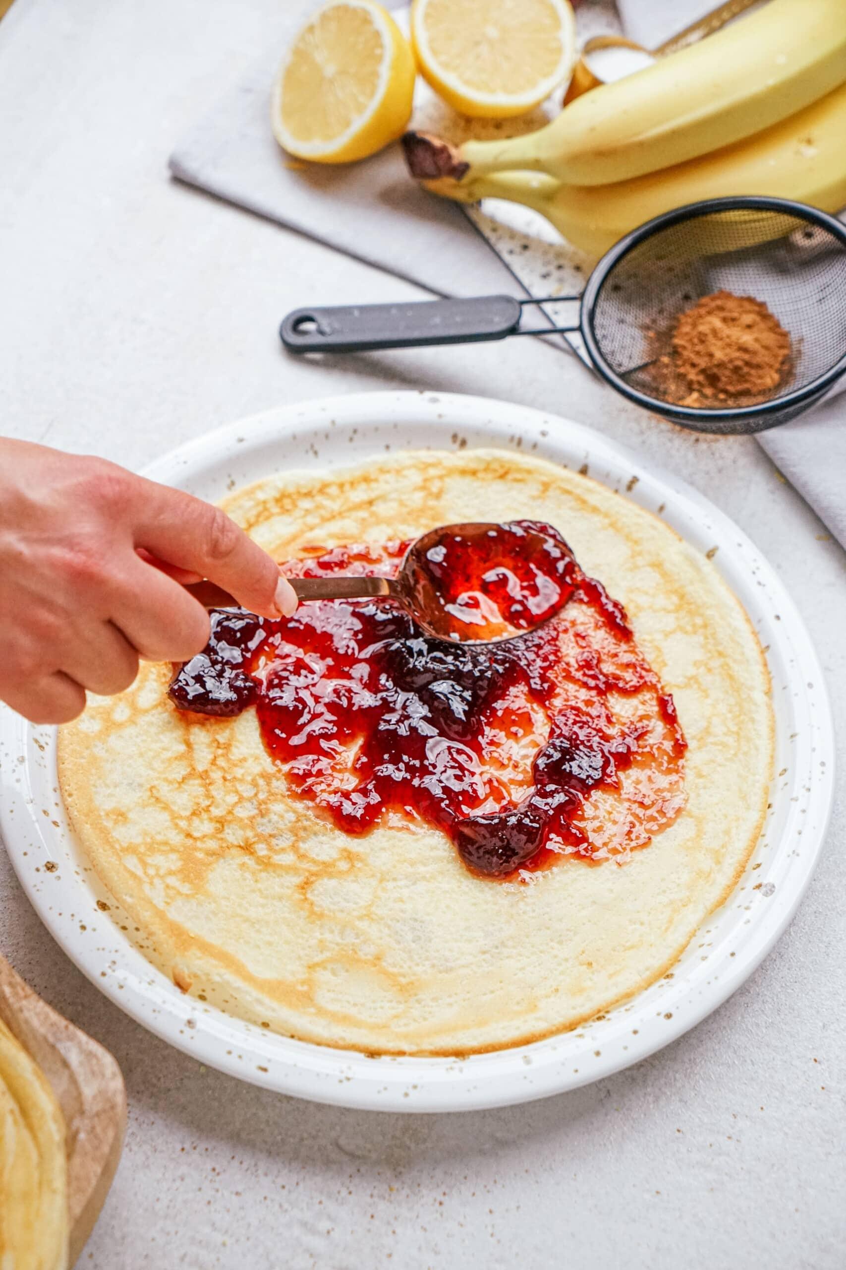 woman's hand spreading jam onto a crepe