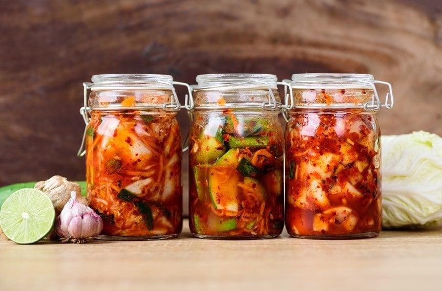 Three jars of kimchi next to its raw ingredients