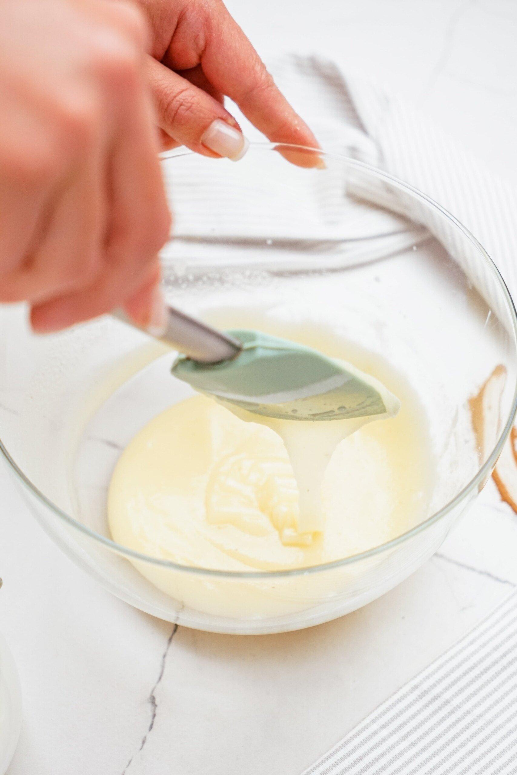 woman's hand using a rubber spatula to stir milk into frosting mixture